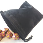 Large black dice bag with dice rolling out on a white background.  